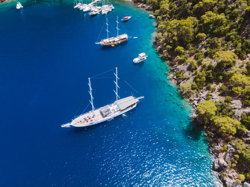 Aerial drone perspective of luxury Turkish gulets and yachts in the deep blue and turquoise waters of the mediterranean sea. The bay and cliffs protect the boats from the strong winds.