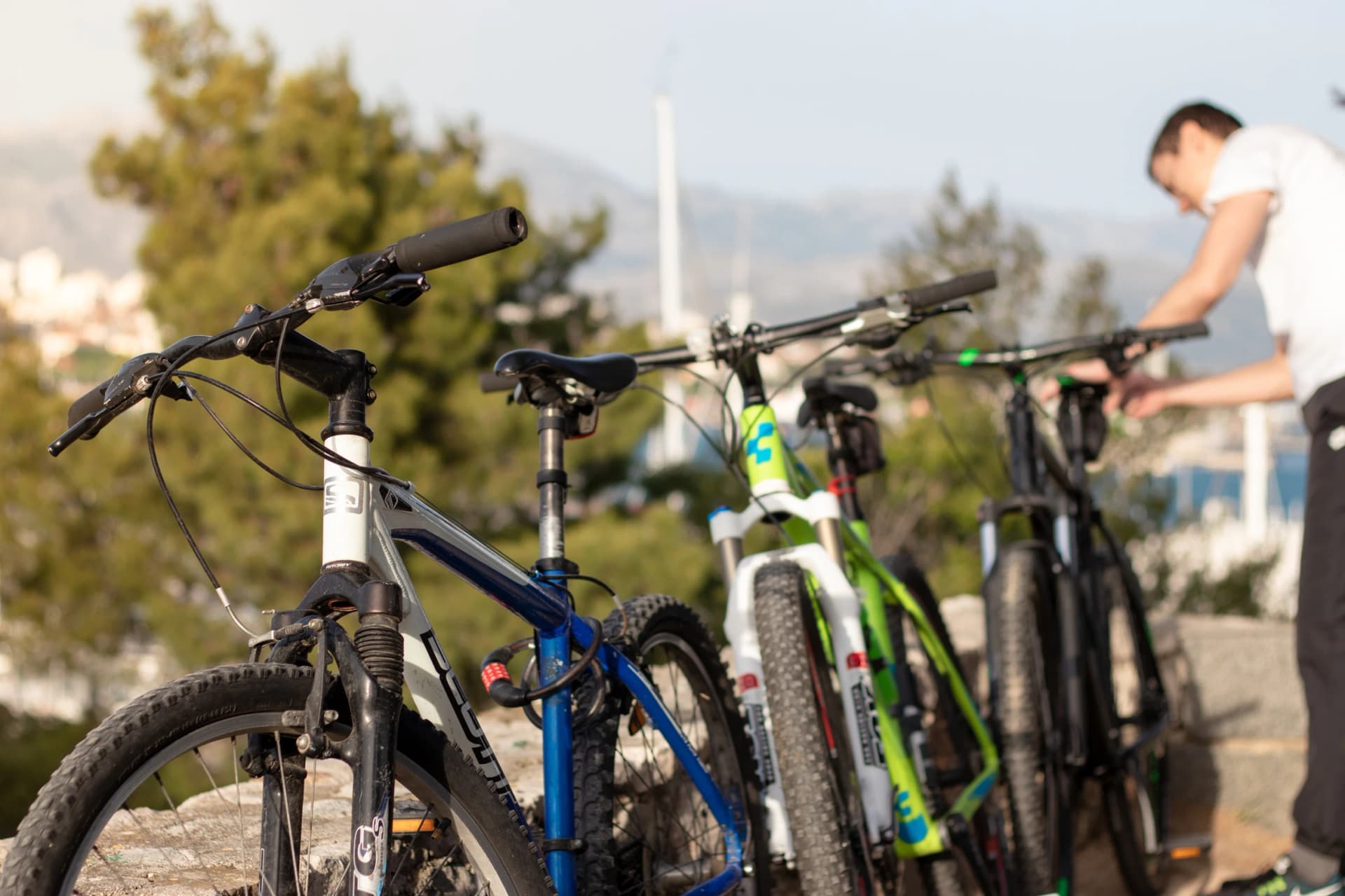 Split,Croatia May 2020 Blue green and black mountain bikes standing on a wall. Scott and Cube branded popular bikes, man fiddling with the last bike. Day spend outside in nature