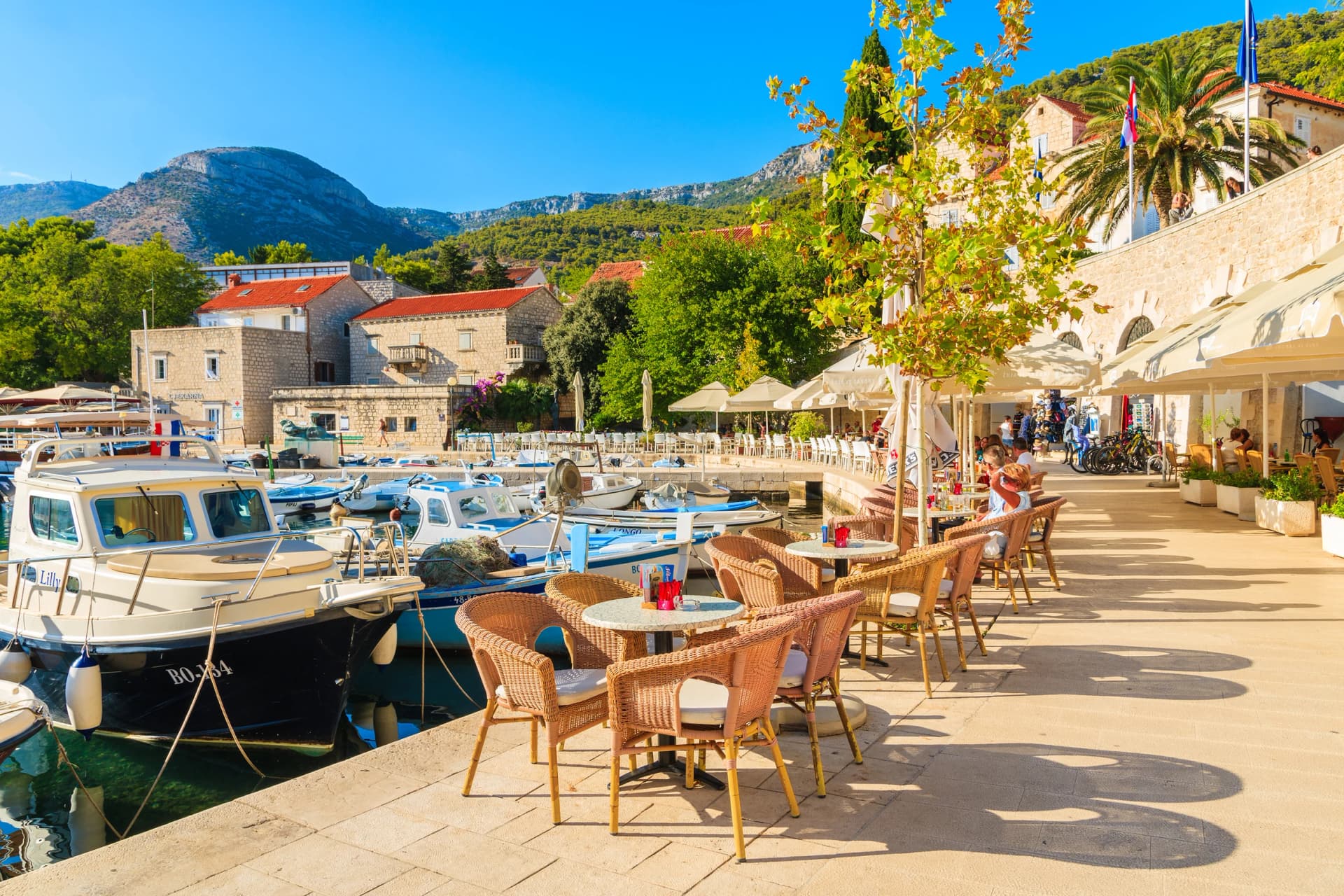 BOL PORT, BRAC ISLAND - SEP 14, 2017: restaurant tables in Bol port with fishing boats on late summer afternoon, Brac island, Croatia.