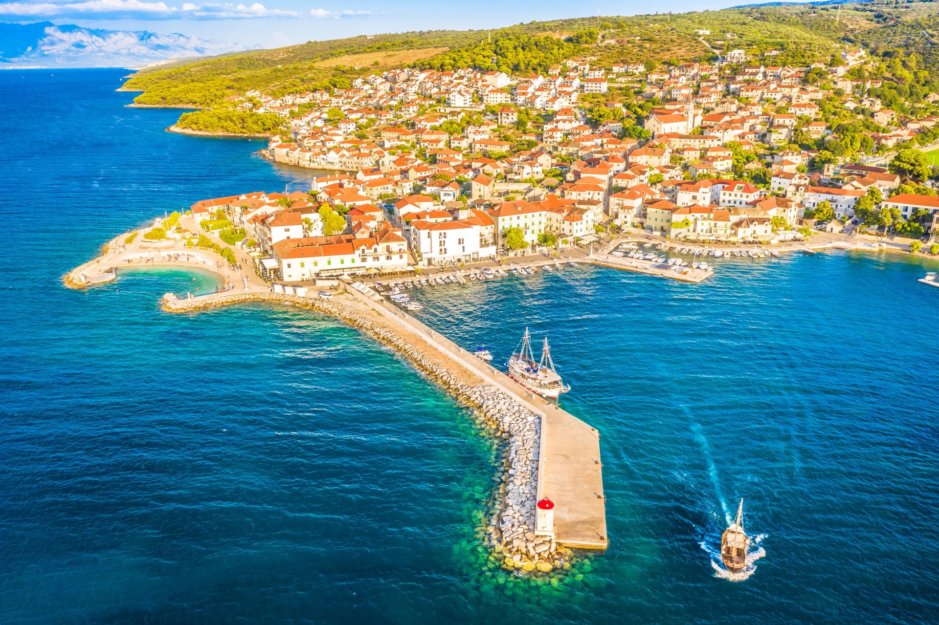 A stunning aerial view of Postira Riva on Brac Island, Croatia, captured on a summer afternoon, showcasing its charming waterfront, traditional stone buildings, and the crystal-clear Adriatic Sea