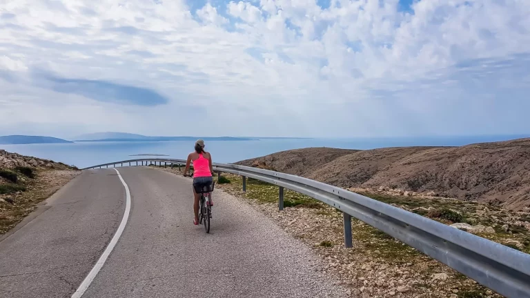 Een meisje in een sportieve outfit rijdt op een fiets over een steile weg in de Middellandse Zee. Meisje geniet van de rit. Dikke wolken boven. Actieve vakantie. Mooie kustlijn van Kroatië